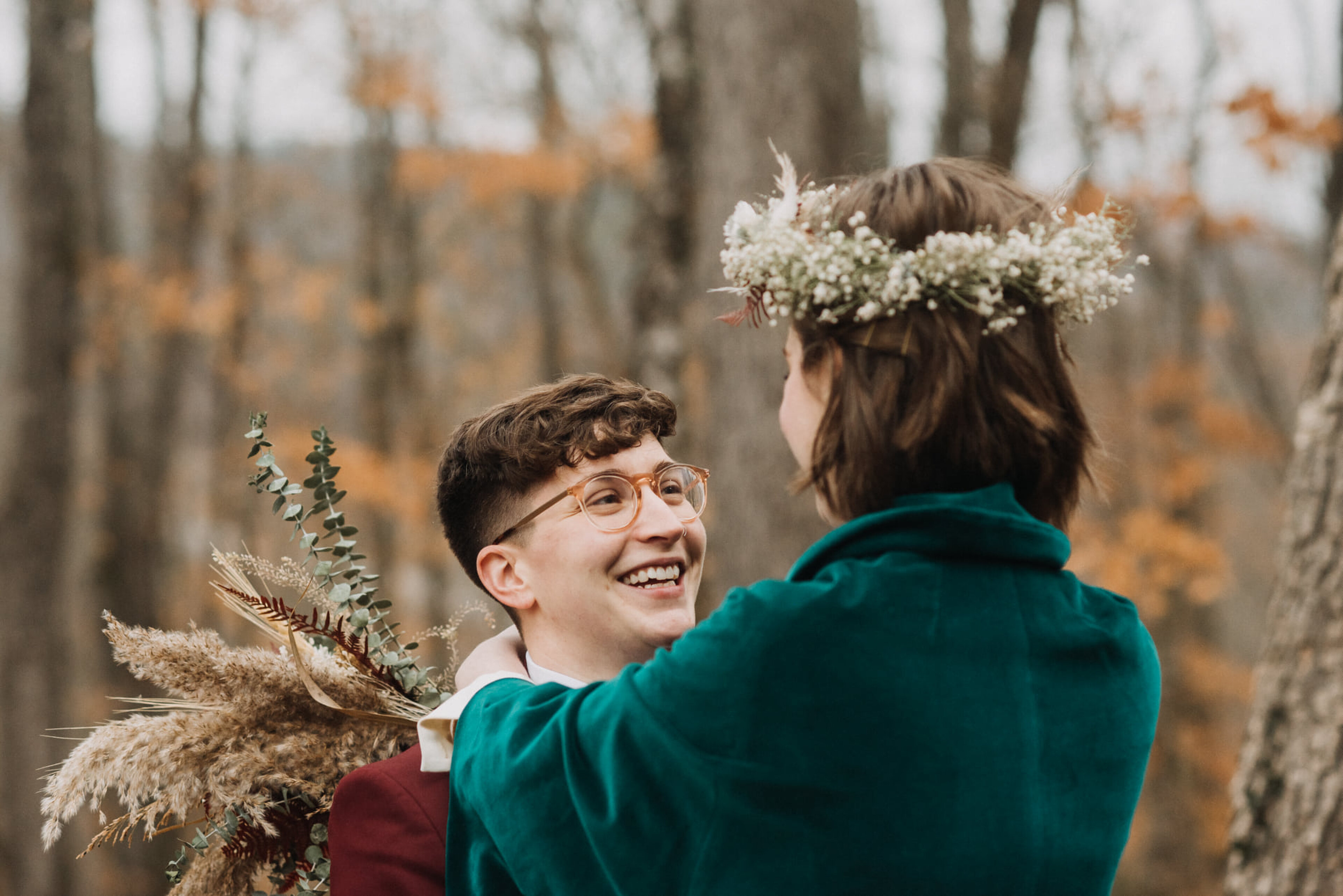 Wedding couple laughing together in the forest with a floral crown, velvet green jacket, and dried bouquet