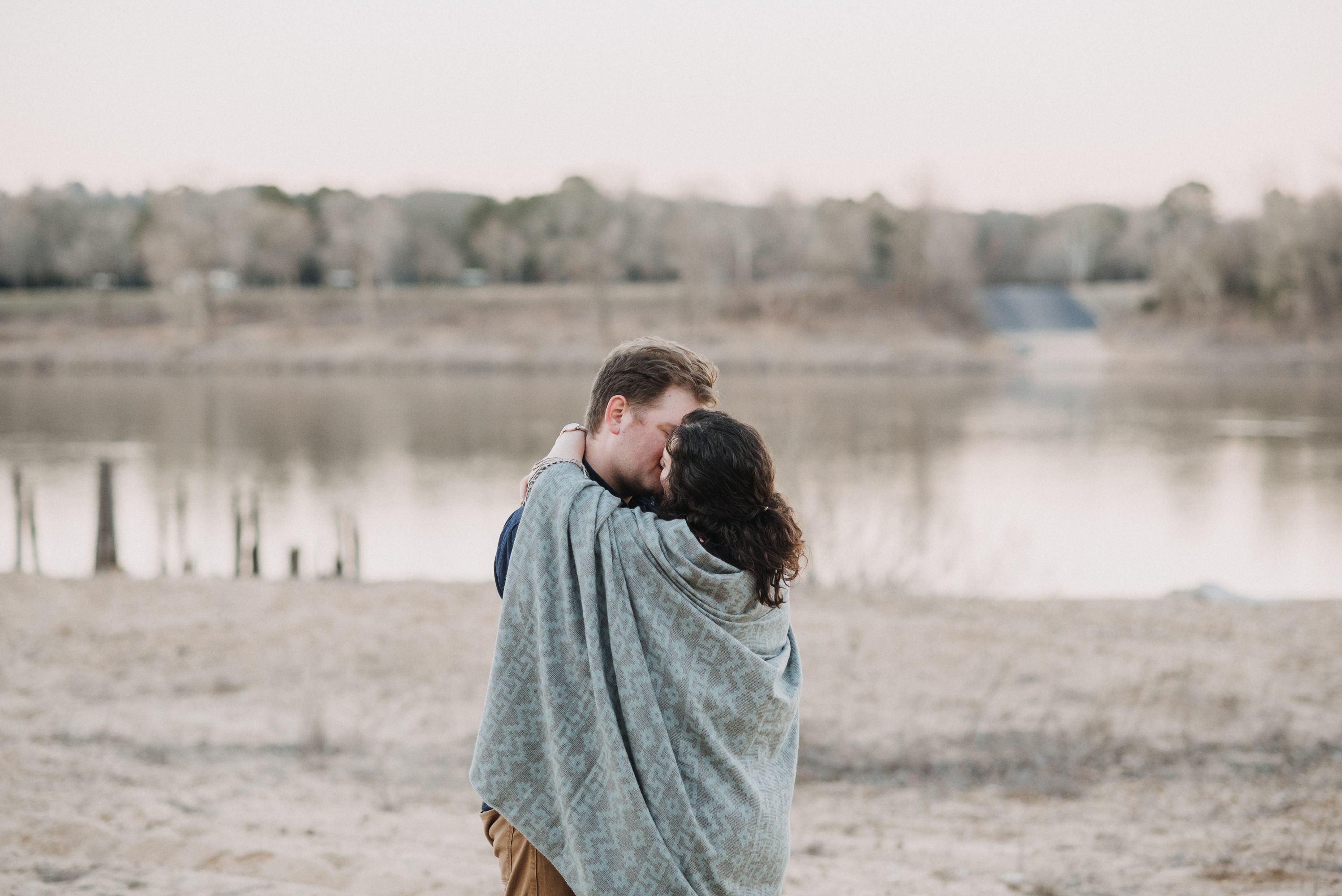 Emily and Noel kissing under a blanket by the lake at Lock and Dam State Park in Russellville Arkansas