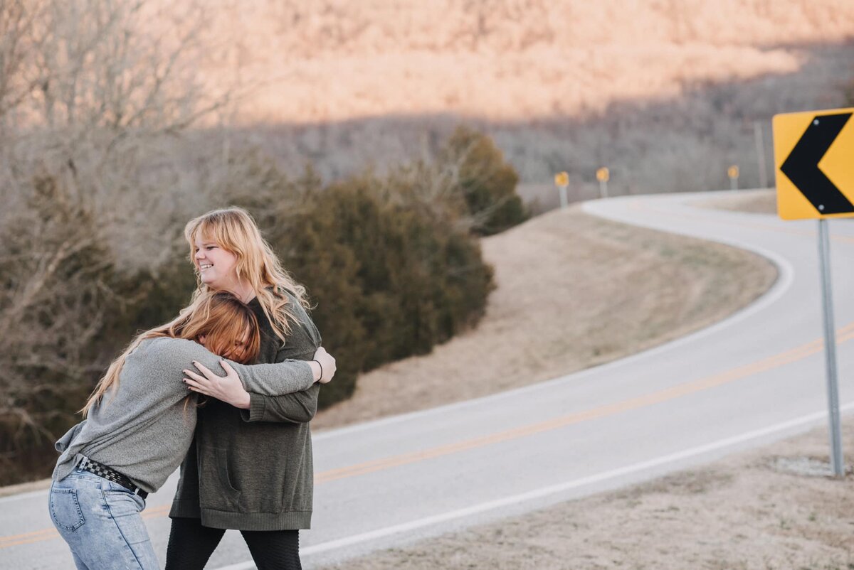 Mia Quain smiling while hugging Decidua beside a winding road in soft golden light